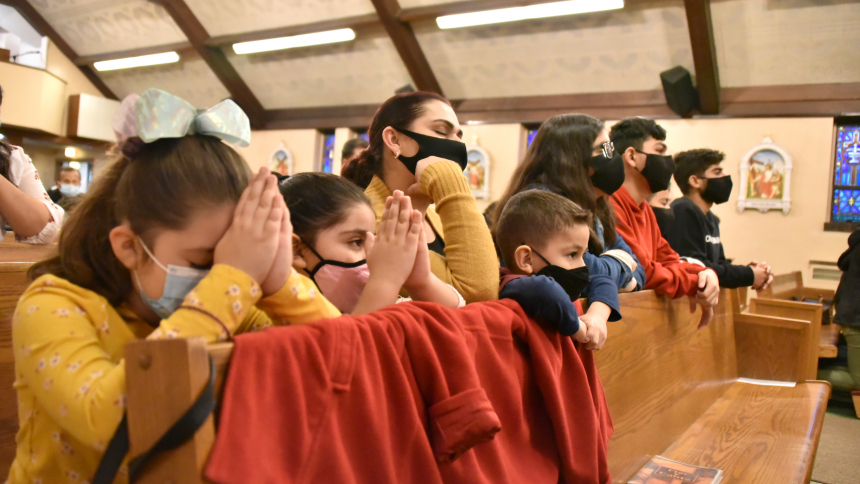 family wearing masks prays in a pew