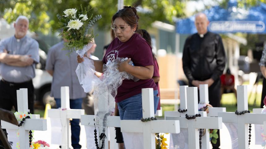 A woman places flowers among crosses in a memorial set up outside Robb Elementary School in Uvalde, Texas, to honor the 19 students and two teachers killed there May 24, 2022, in a mass shooting. People gathered at the memorial May 24, 2023, one year after the shooting. Father Daniel Carson, the pastor of St. Peter's Parish on Capitol Hill in Washington seen at right in the background of this photo, joined people praying there. He was among 14 parish leaders from across the United States who participated in