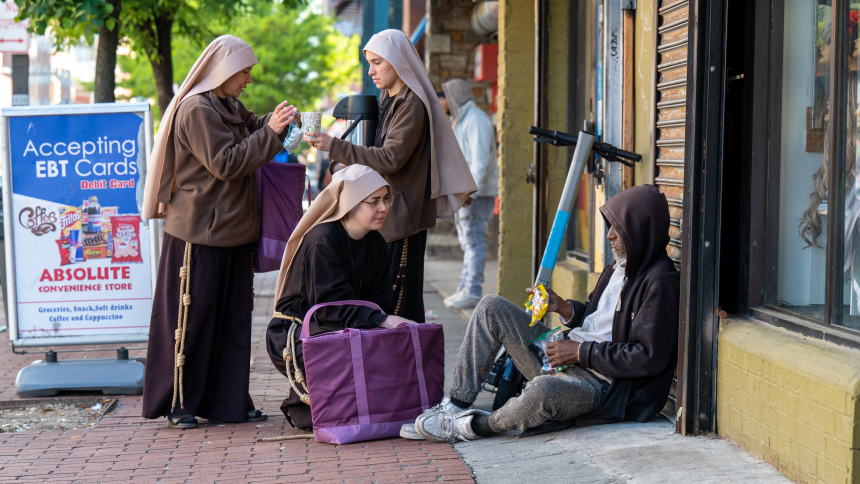 Sister Giovana of the Most Holy Name of Jesus (squatting) joins Sister Samaritan of Scourged Love (left) and Sister Maria Clara of the Crucified in giving food to a man near Lexington Market in Baltimore May 3, 2023. (OSV News Photo/Kevin J. Parks, Catholic Review)