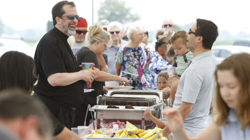 Father Mick Kopil, pastor of St. Elizabeth Ann Seton Catholic Church visits with parishioners as they make their way through the food line during the parish picnic on July 16. (Bob Wellinski photo)