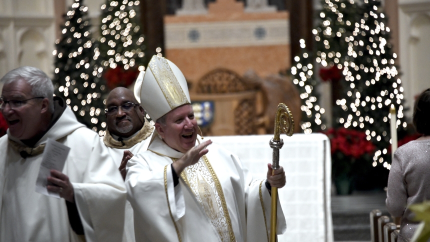 During the recessional procession, Bishop Robert J. McClory (front, right) smiles as he blesses the faithful and is preceeded by Father Michael Surufka (left), O. F. M., rector of the Cathedral of the Holy Angels, and followed by Deacon Martin Brown (center), at the Christmas Eve vigil Mass on Dec. 24 in Gary. (Anthony D. Alonzo photo)