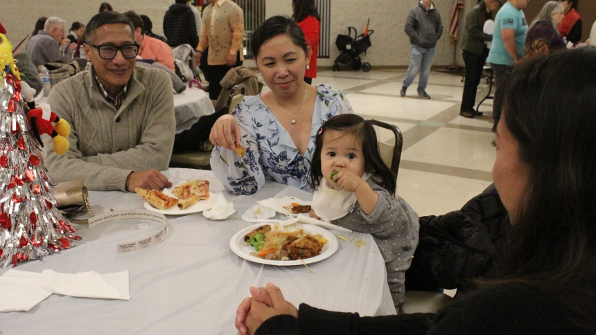 Parents Kyle and Michelle Carlay, of St. John, and (at right) aunt Irene Copak, of Crown Point, watch young Maya Carlay taste broccoli along with some traditional Filipino foods at the Simband Gabi dinner held at Our Lady of Consolation in Merrillville on Dec. 16. Close to 100 people enjoyed lumpla (egg rolls), picadillo (beef over rice) and pancit (chicken and rice noodles); those looking for traditional American fare munched on pizza and baked chicken. The family was happy to be sharing their culture and 