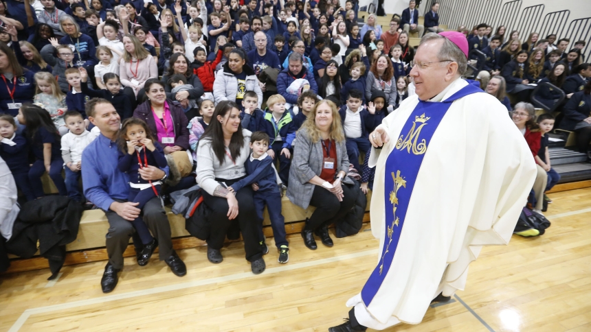 Bishop Robert J. McClory passes by students Queen of Saints students as he randomly picked students to answer questions as part of his homily during the Catholic Schools Week All City Mass in Marquette’s Scholl Center on January 29. (Bob Wellinski photo)