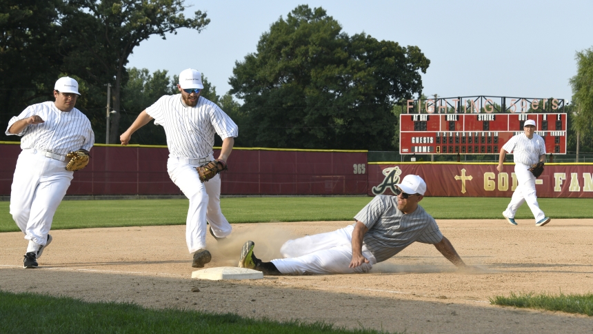 Father Christopher Stanish, vicar general and moderator of the curia, slides into third base ahead of the tag by Seminarian Ryan Pierce as fellow discerner Nicholas Emsing (left) and Deaacon Alexander Kouris (right) look on during the inaugural Collars versus Scholars softball game at Andrean High School's baseball field in Merrillville on July 12. The softball contest between diocesan priests and seminarians, where the Collars prevailed over the Scholars 12-6, was a public event sponsored by the diocesan v