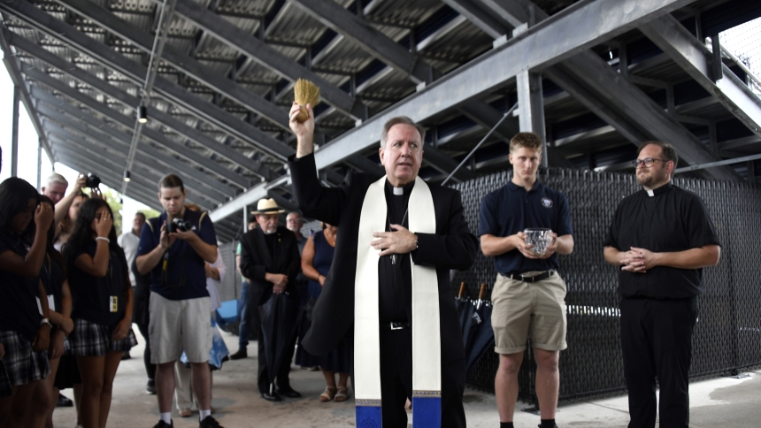 Bishop Robert J. McClory (front) whisks holy water as he offers a blessing before Bishop Noll Institute student-athletes at the Warriors' new football, soccer and track facility in Hammond on the Solemnity of the Assumption of the Blessed Virgin Mary, Aug. 15. Rainy conditions precluded a back-to-school liturgy at the school's new 1,400-seat stadium, so the faithful gathered in the fieldhouse. (Anthony D. Alonzo photo)