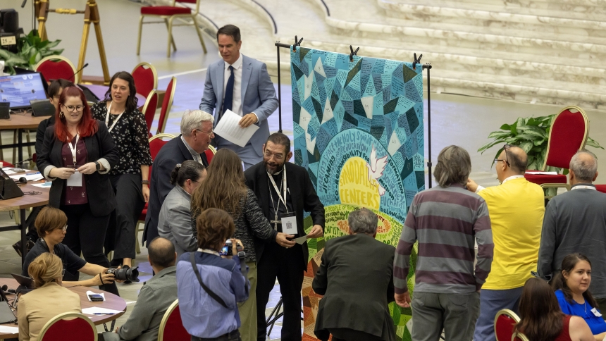 Bishop Daniel E. Flores of Brownsville, Texas, center, speaks to the artist who made a mosaic with thoughts about the Synod of Bishops and prayers for the synod written by U.S. university students as Cardinal Mario Grech, kneeling, adds his prayer to the mosaic in the Paul VI Audience Hall at the Vatican Oct. 18, 2024. (CNS photo/Pablo Esparza)