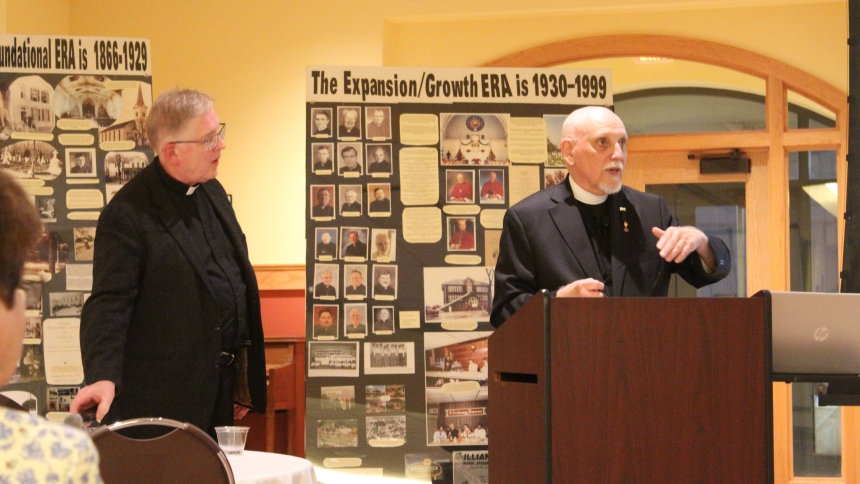 With dozens of photos gathered by the St. Michael Parish 150th Anniversary Committee on display, Father Martin Dobrzynski (left), pastor, listens to Father Dominic Bertino, historian for the Diocese of Gary, explain the impact the parish has had on the Town of Schererville since it was established in 1874. Father Bertino's presentation was well-attended by parishioners on Sept. 27 as the parish began its celebratory weekend. (Marlene A. Zloza photo)