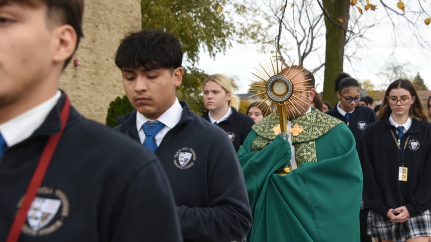 Bishop Noll Institute students surround Father Jeffrey Burton (center), school chaplain, as he processes with the Blessed Sacrament in a monstrance that was blessed by Pope St. John Paul II, at the Hammond school on Nov. 6. The diocesan Serra Club secured the use of the sacred vessel from Oct. 28-Nov. 8, as part of a special 10-stop initiative to encourage prayer for vocations to the priesthood and religious life. (Anthony D. Alonzo photo)