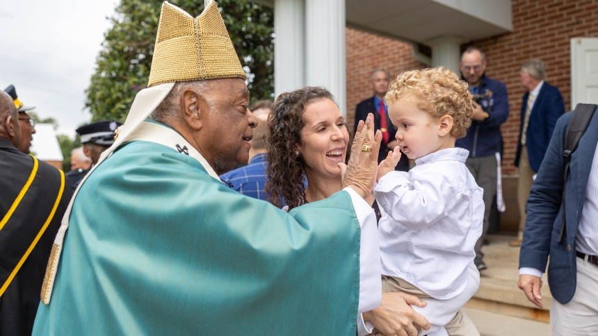 After celebrating a 350th anniversary Mass for St. Mary Parish in Newport, Md., on Sept. 7, 2024, Washington Cardinal Wilton D. Gregory greets parishioners outside the church and plays Patty-Cake with a little boy, Gregory Skibinsky, held by his mother, Erica Skibinsky. (OSV News photo/Mihoko Owada, Catholic Standard)