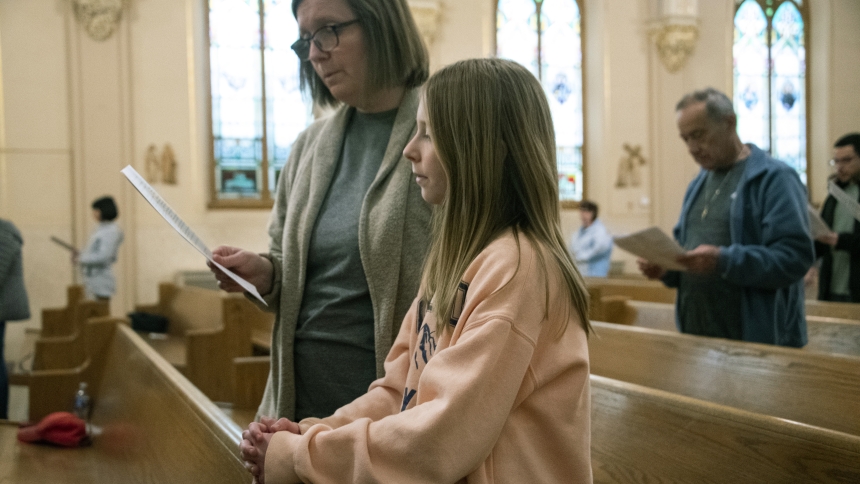 Jackie Keenan (left) prays from a program along with her daughter Mary Keenan (right), 10,  and are among those gathered at St. Joseph church in Dyer at a Holy Hour featuring silent Eucharistic adoration, hymns, Rosary, litanies, and benediction on March 13. Deacon Gary Blue presided and Jake Keenan, 12, served on the sanctuary. (Anthony D. Alonzo photo)