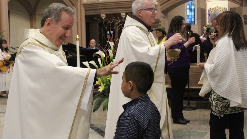 During Easter Sunday Mass on April 20 at the Cathedral of the Holy Angels, Bishop Robert J. McClory (left) blesses a young celebrant while Father Michael Surufka, O.F.M., distributes the Holy Eucharist. (Marlene A. Zloza photo)