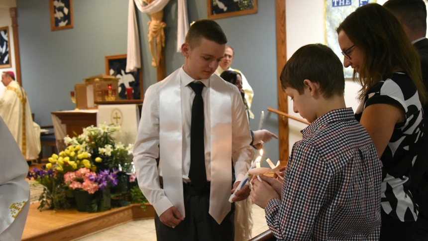 After being baptized, Cale Mendenhall (center) uses his sacramental candle to light the votive lamps of family members during the Easter Vigil on April 19, at St. Teresa of Avila Catholic Student Center in Valparaiso. Seven individuals formally joined in full communion with the Catholic Church before a capacity congregation of worshipers. (Anthony D. Alonzo photo)