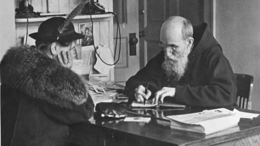 Blessed Solanus Casey is pictured taking a note from a woman who visited him at St. Bonaventure Monastery in Detroit in 1941. The Capuchin Franciscan friar kept dozens of notebooks filled with prayer requests and favors from the thousands who visited him each year. (OSV News photo/Archdiocese of Detroit)  