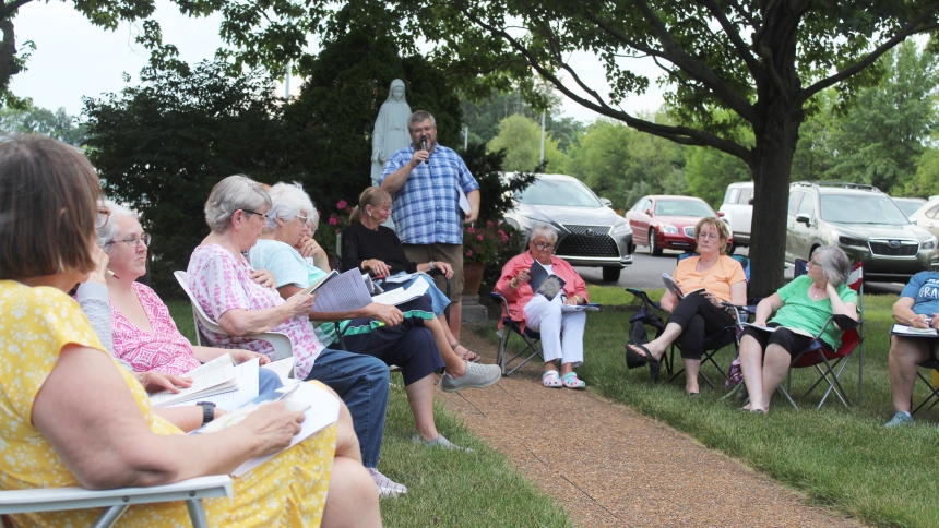 Meeting under the watchful eye of a statue of the Blessed Mother on the church campus, Father Ian Williams (standing), priest-in-residence at St. Helen in Hebron guides the Gazebo Reflections group in a discussion of inspirational saints on June 30. The group is meeting biweekly on Mondays through Aug. 25 to share their thoughts about the book “33 Days to Eucharistic Glory” by Matthew Kelly, with the next session set for July 14 at 6 p.m. book “33 Days to Eucharistic Glory” by Matthew Kelly,