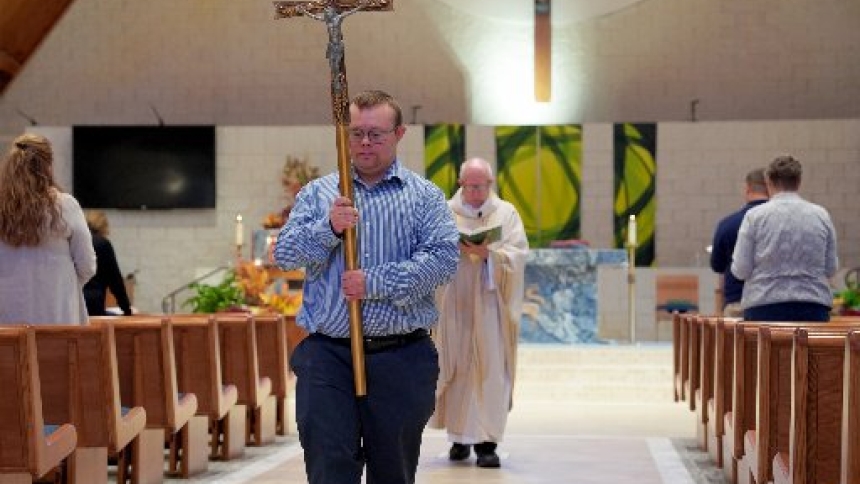 Robby Heil, 26, a liturgical minister at St. James Parish in Novi, Mich., who has Down syndrome, carries the cross during Mass Sept. 8, 2025. Robby is a regular volunteer during parish Masses and is a well-known fixture at St. James, said Father Ed Zaorski, pastor, Robby's friend and mentor. Although Robby's story has been told in several local news outlets, his biggest impact is at his parish, said his father, Charles Heil. (OSV News photo/Gabriella Patti, Detroit Catholic)