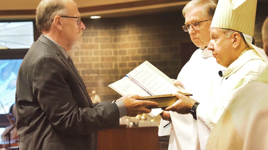 Diaconate candidate Bruce Garwood receives the book of Sacred Scripture as his is instituted as lector by Bishop Robert J. McClory with Father Marty Dobrzynski looks on. Four other men were instituted during the Deacon Jubilee Mass and Institution to the Ministry of Lector on Sept. 18 at St. James the Less. (Deacon Bob Wellinski photo)
