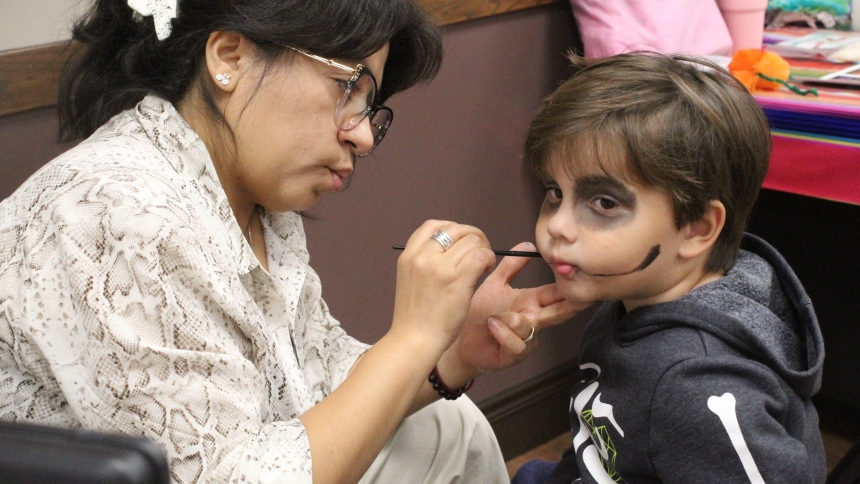 Maria Janes, an artist, paints the face of three-year-old Ezra Aguilar, son of Joel and Nicole Aguilar, of Crown Point, during the Dia de los Muertos celebration on Oct. 18 at Holy Name of Jesus in Cedar Lake. According to information exhibited at the event in Sacred Heart Hall, “face painting turns the living into joyful symbols of the dead.” Wearing a “calavera” design shows that life and death are forever joined. . (Marlene A. Zloza photo)