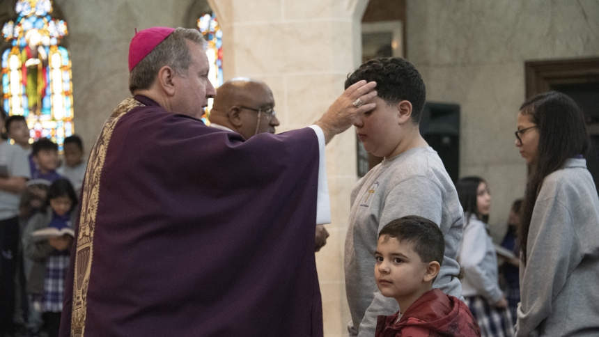 St. Casimir fifth-grader Levi Kaminsky (second from right) receives ashes as he accompanies pre-kindergartener Jacob Lagunas  (bottom), who has also been imposed with ashes by Bishop Robert J. McClory (left), during Mass on March 5, Ash Wednesday, at the Hammond parish. During his homily, Bishop McClory told the youthful gathering, "I guarantee when you make those commitments to (Lenten prayer, fasting and almsgiving) and get back in the game a little more, you may have an amazing Lent and receive even more