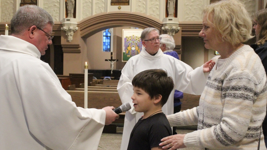 Catechumen Michael Shea (center), of Merrillville, a student at Aquinas Catholic Community School, states his name for Bishop Robert J. McClory and the congregation at the Rite of Election service on Feb. 22 at the Cathedral of the Holy Angels in Gary. At left is Father Peter Muha, who held the microphone for the catechumens, and at right is Marie Wilson, Michael’s sponsor and the office manager at the Merrillville school. (Marlene A. Zloza photo)