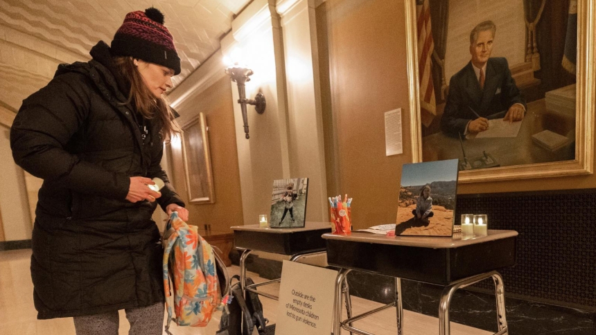 Jackie Flavin, mother of Harper Moyski, who died in the Aug. 27, 2025, shooting at Annunciation Church in south Minneapolis, looks at desks she set up Feb. 23, 2026, in honor of Harper and another Annunciation student, Fletcher Merkel, who also died in the shooting. Flavin and other Annunciation volunteers set up those two desks plus others outside the Minnesota capitol building to signify children who have died by gun violence in Minnesota since 2021. They are part of an organization of parents called Annu