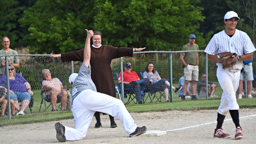 Sister Mary Amata Naville, OSF, (center) signals that the runner, Father Alexander Kouris (front), is safe at third base as seminarian John LaCorte (right) walks away during the Collars vs. Scholars Classic, hosted on July 10 at the Marquette Athletic Complex in Michigan City. The annual recreational event brings out a competitive spirit in the clergymen and discerners who participate, but is mainly designed to encourage support for priestly vocations from among area faithful. (Anthony D. Alonzo photo)