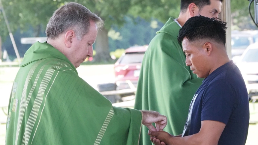 Bishop Robert J. McClory distributes communion, along with Father Roque Meraz during the Mass for Migrant Workers at Garwood Orchards on July 12. (Michael Wellinski photo)