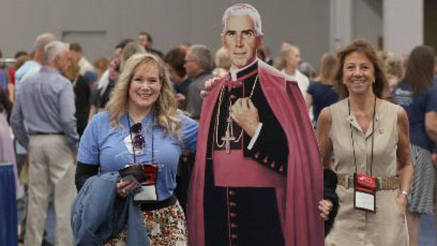 Women carry a cutout of Venerable Fulton J. Sheen in the exhibit hall ahead of the beatification Mass for Archbishop Sheen Sept. 24, 2026, at The Dome at America's Center in St. Louis. The archbishop is remembered as one of the most influential and innovative evangelists in American history. (OSV News photo/Bob Roller)
